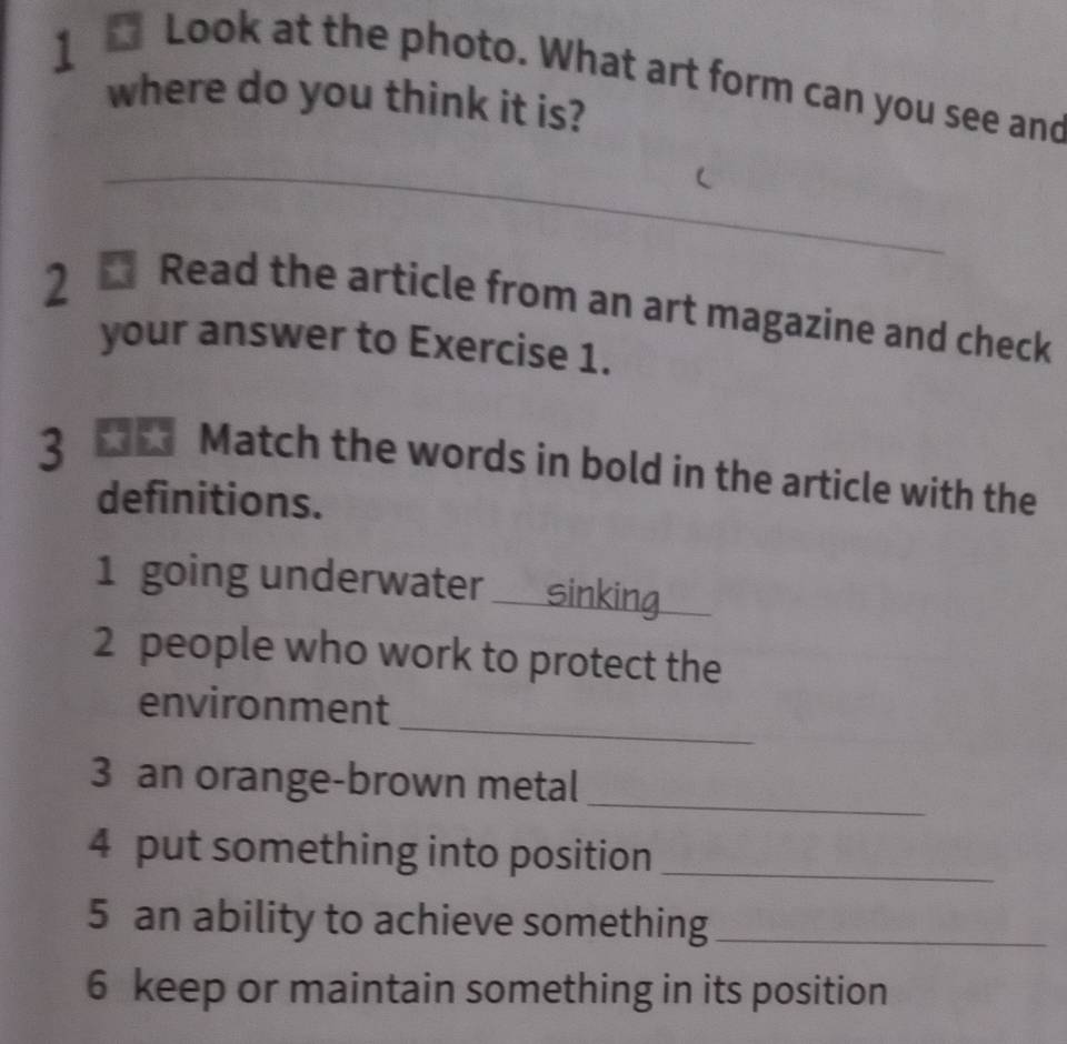 Look at the photo. What art form can you see and 
where do you think it is? 
_ 
2 
Read the article from an art magazine and check 
your answer to Exercise 1. 
3 t Match the words in bold in the article with the 
definitions. 
1 going underwater __ sinking 
2 people who work to protect the 
_ 
environment 
3 an orange-brown metal 
_ 
4 put something into position_ 
5 an ability to achieve something_ 
6 keep or maintain something in its position