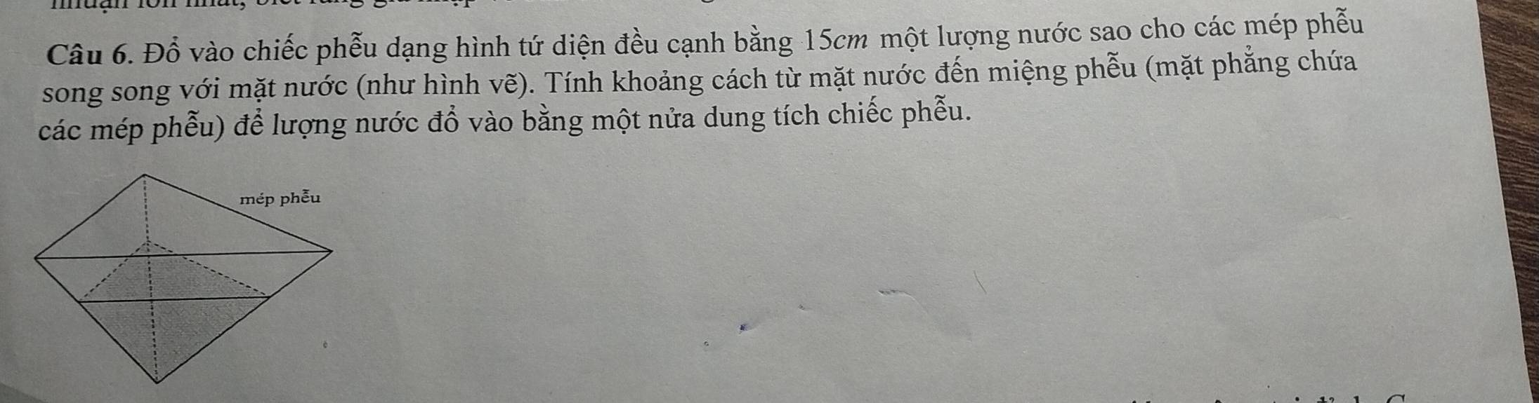 Đổ vào chiếc phễu dạng hình tứ diện đều cạnh bằng 15cm một lượng nước sao cho các mép phẫu 
song song với mặt nước (như hình vẽ). Tính khoảng cách từ mặt nước đến miệng phễu (mặt phẳng chứa 
các mép phễu) để lượng nước đổ vào bằng một nửa dung tích chiếc phễu.