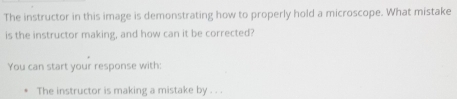 The instructor in this image is demonstrating how to properly hold a microscope. What mistake 
is the instructor making, and how can it be corrected? 
You can start your response with: 
The instructor is making a mistake by . . .